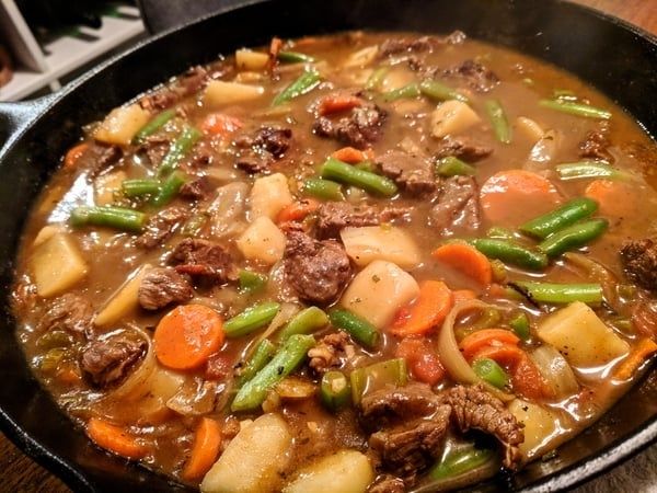 Mustig köttgryta med morötter, potatis och gröna bönor i en panna